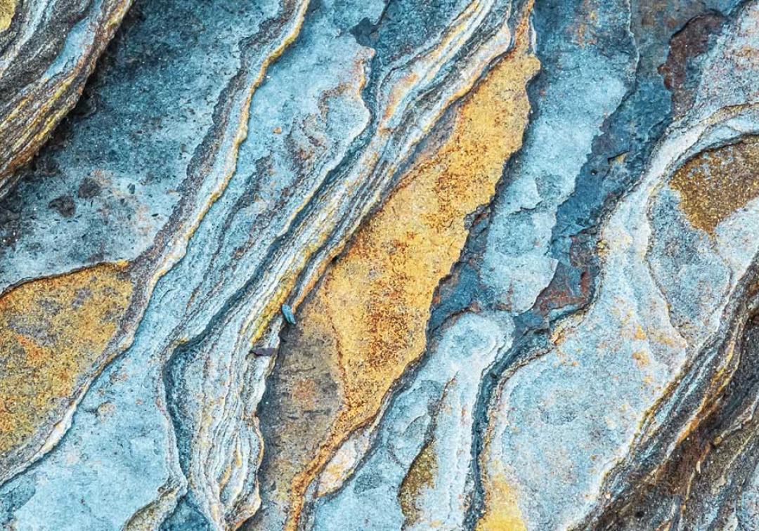 Closeup of blue and gold bands of colour running through a rockface