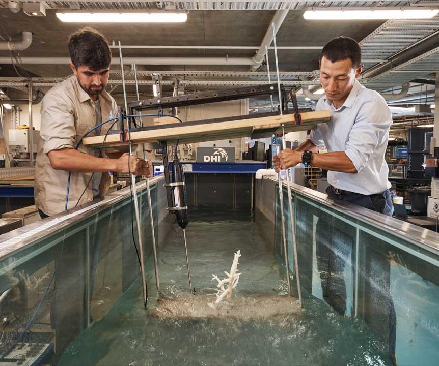 Researchers hold a piece of equipment in a tank of water in a UQ hydraulics lab