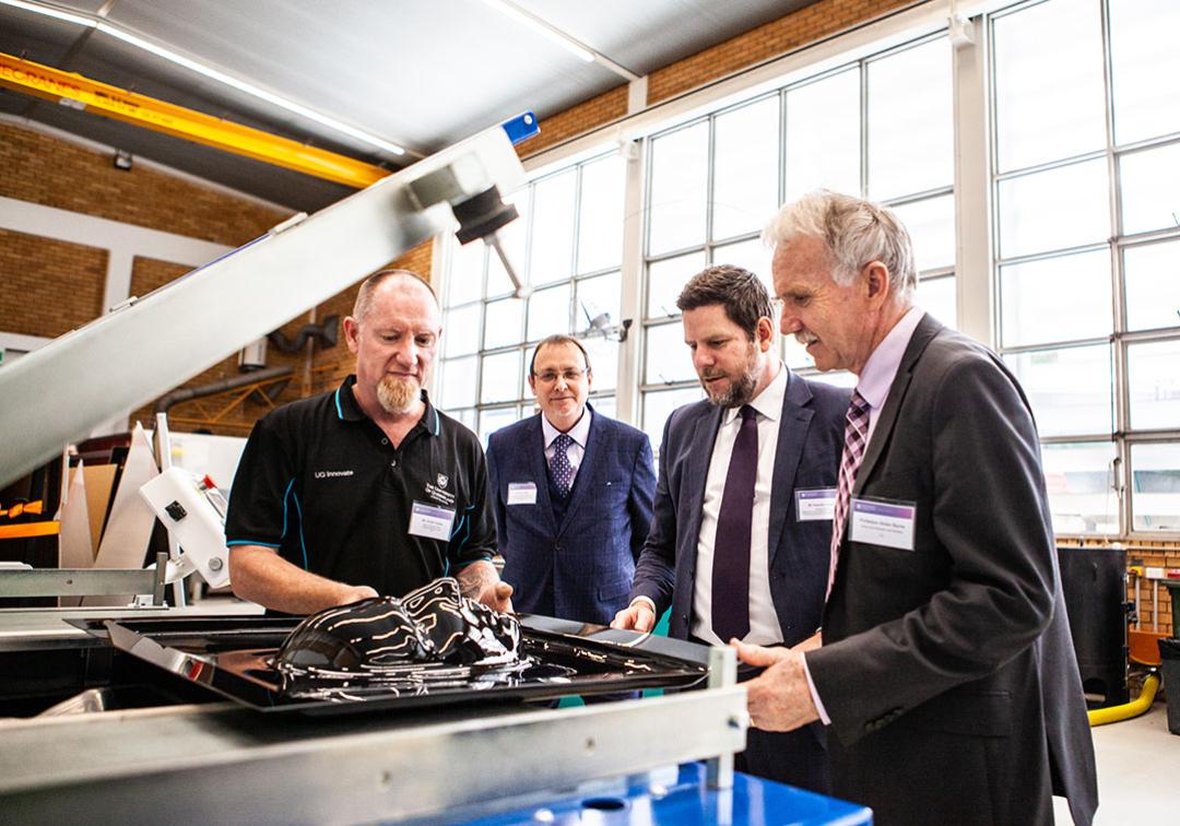 Four men in suits inspecting a piece of research equipment. 