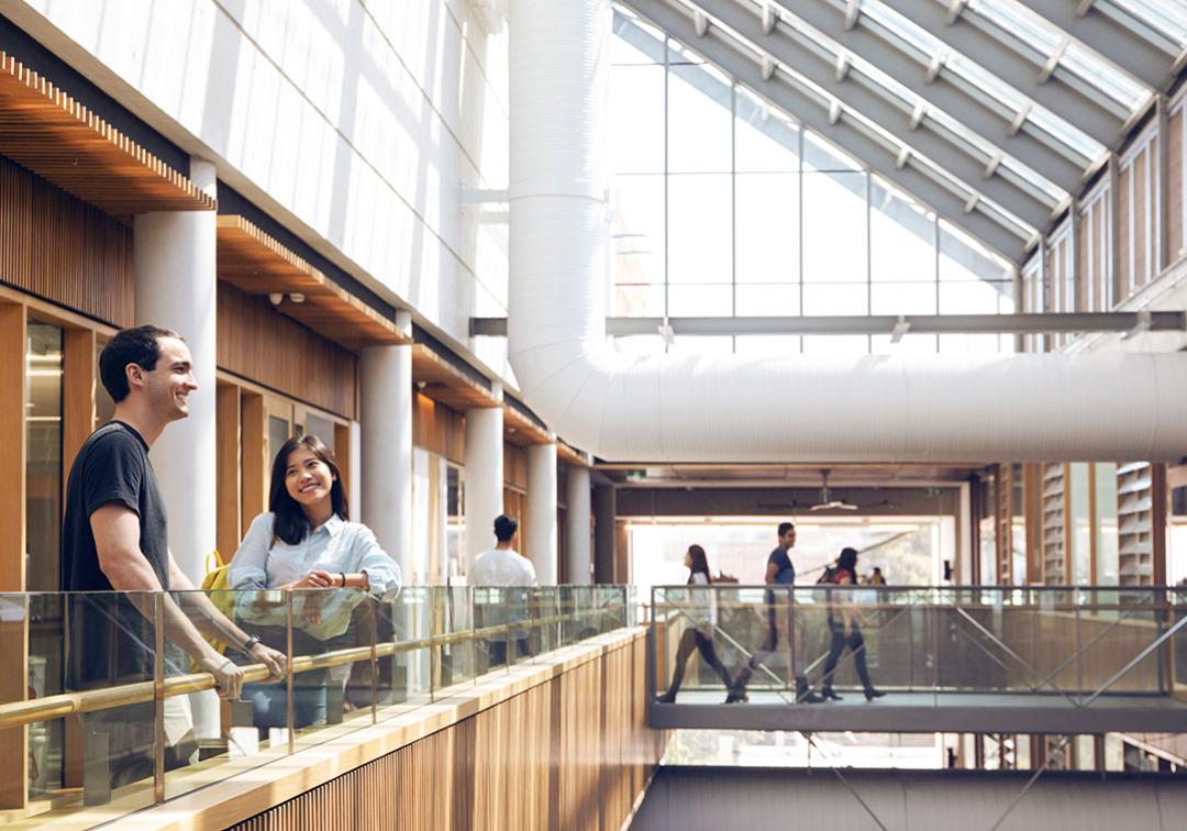 Students standing on the top level of a building with a glass roof above them. 