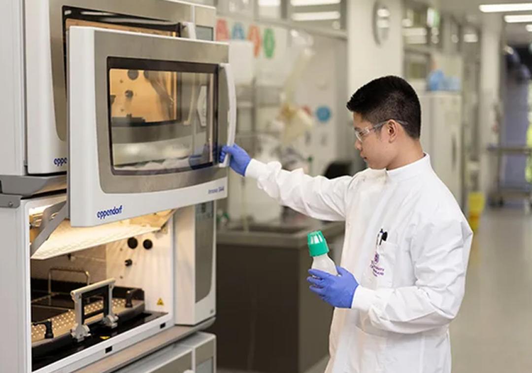 A person wearing a UQ lab coat using equipment in a lab.