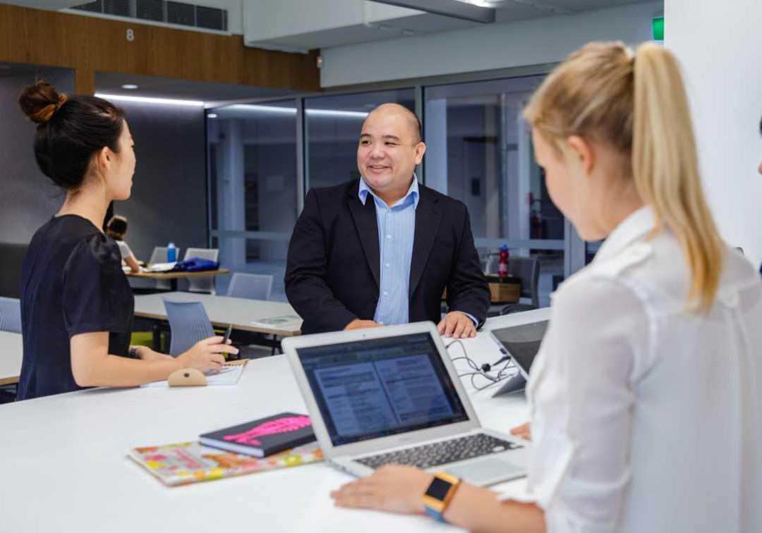 UQ students with laptops and notebooks in conversation with a man in a suit