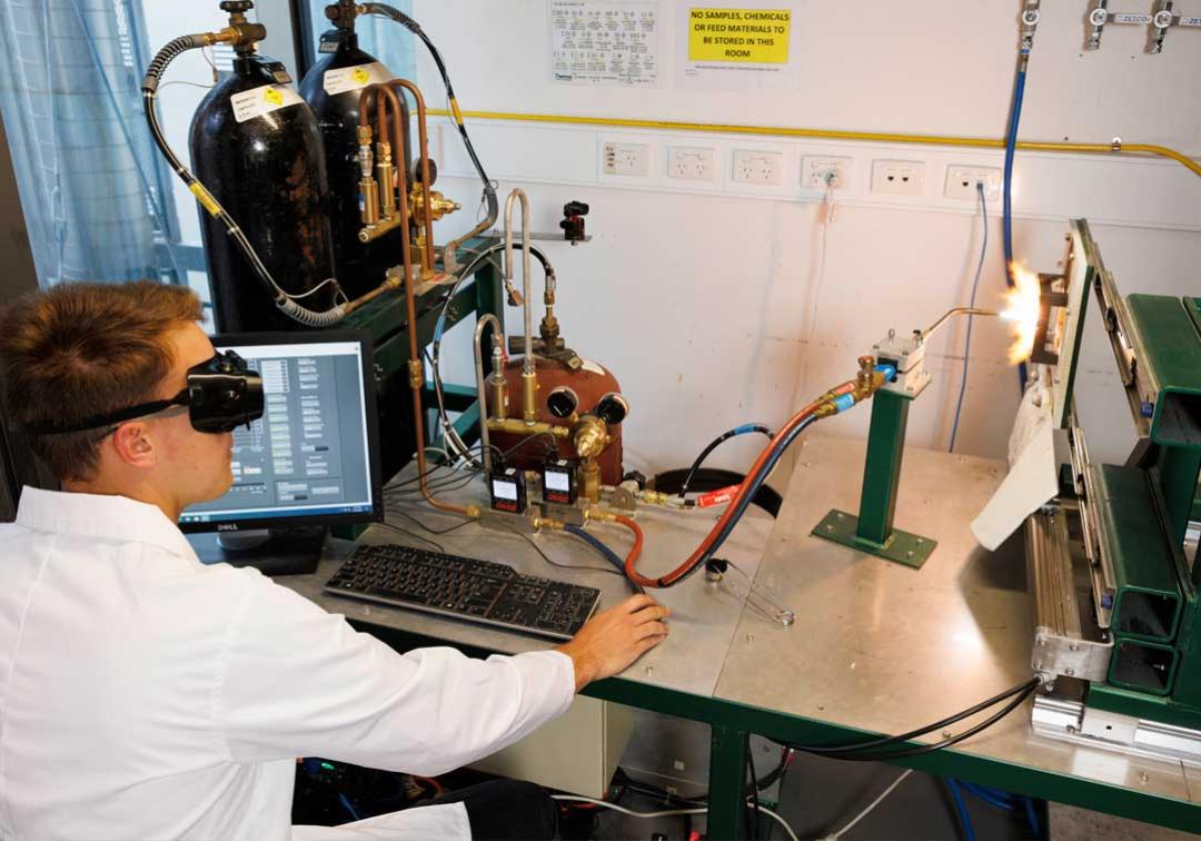 UQ researcher sits at a desk in front of a series of gas tanks and tubes with a high temperature instrument