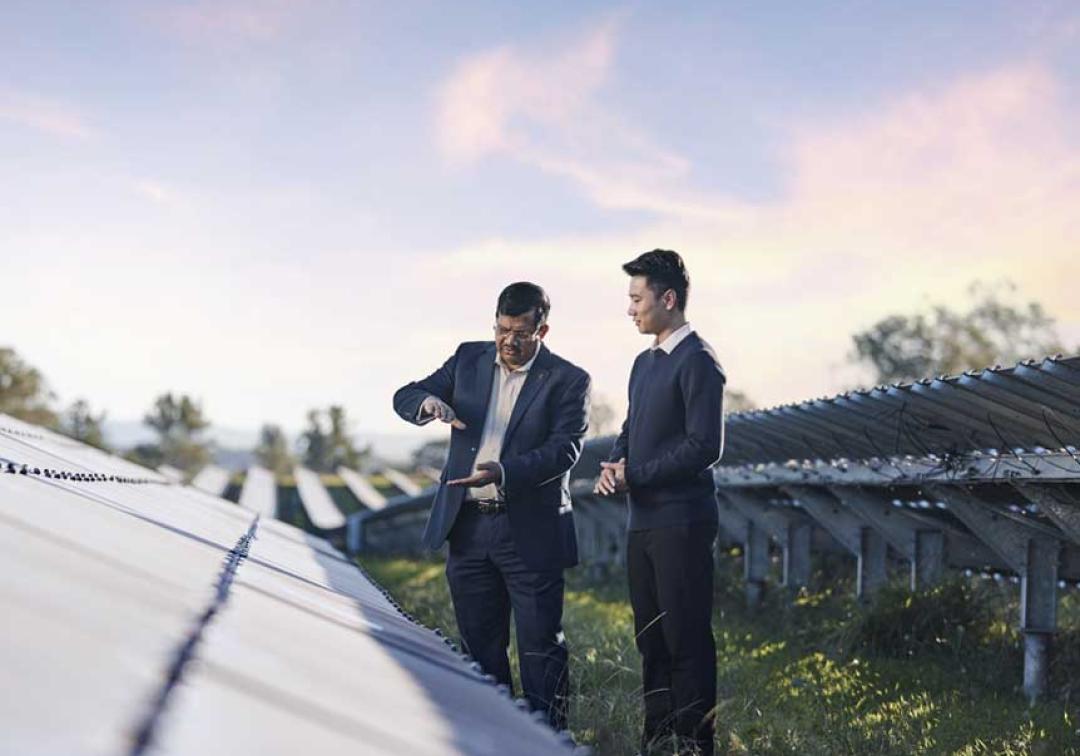 2 UQ researchers assessing a row of solar panels on a sunny day at one of our solar farms