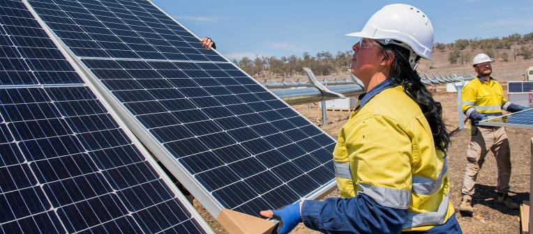 A woman wearing high-vis and a hard hat installs a solar panel.