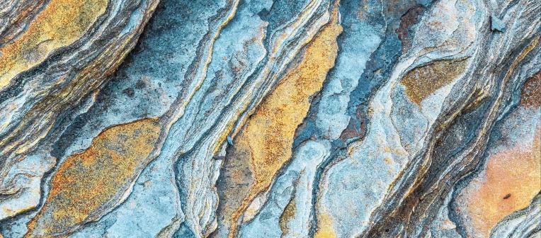 Closeup of blue and gold bands of colour running through a rockface