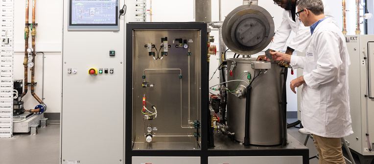 Two scientists in lab coats examine a high temperature furnace