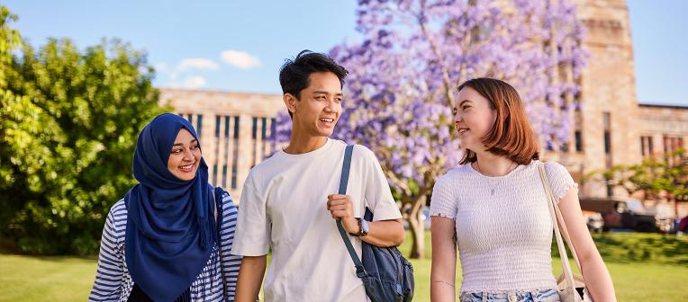 Three people chatting. The sandstone Forgan Smith building and a jacaranda tree in bloom are in the background.