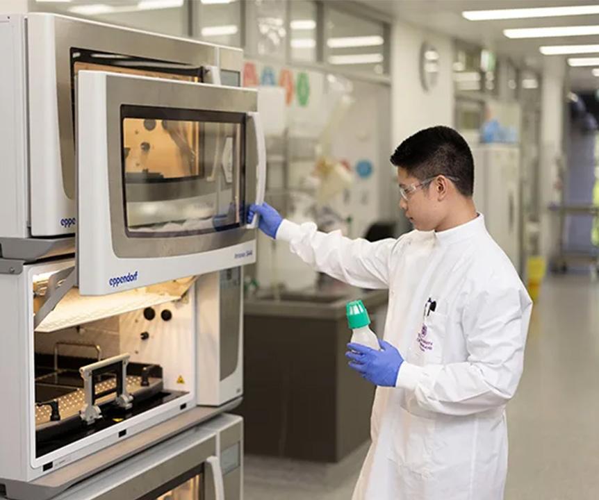 A person wearing a UQ lab coat using equipment in a lab.