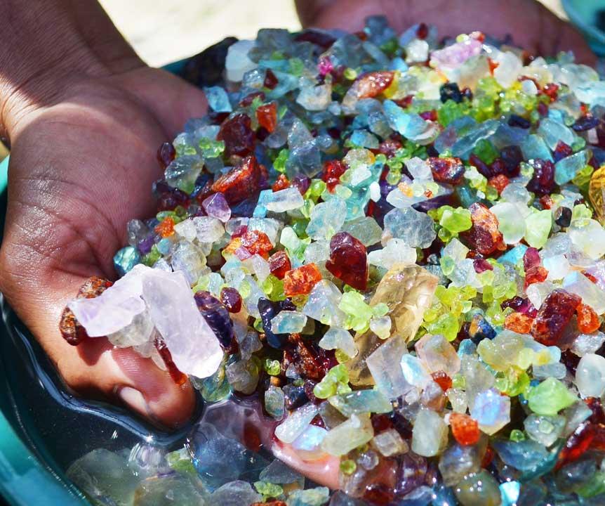 A pair of hands sifts through a bucket of multi-coloured gemstones to extract precious resources.