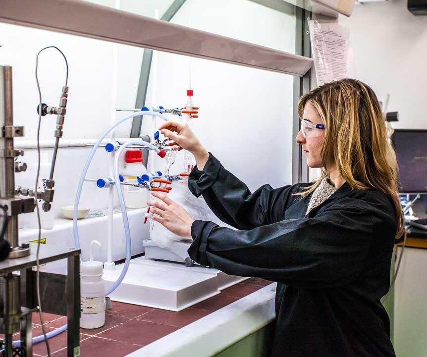 A UQ researcher in a lab investigates a series of tubes and specimen jars.