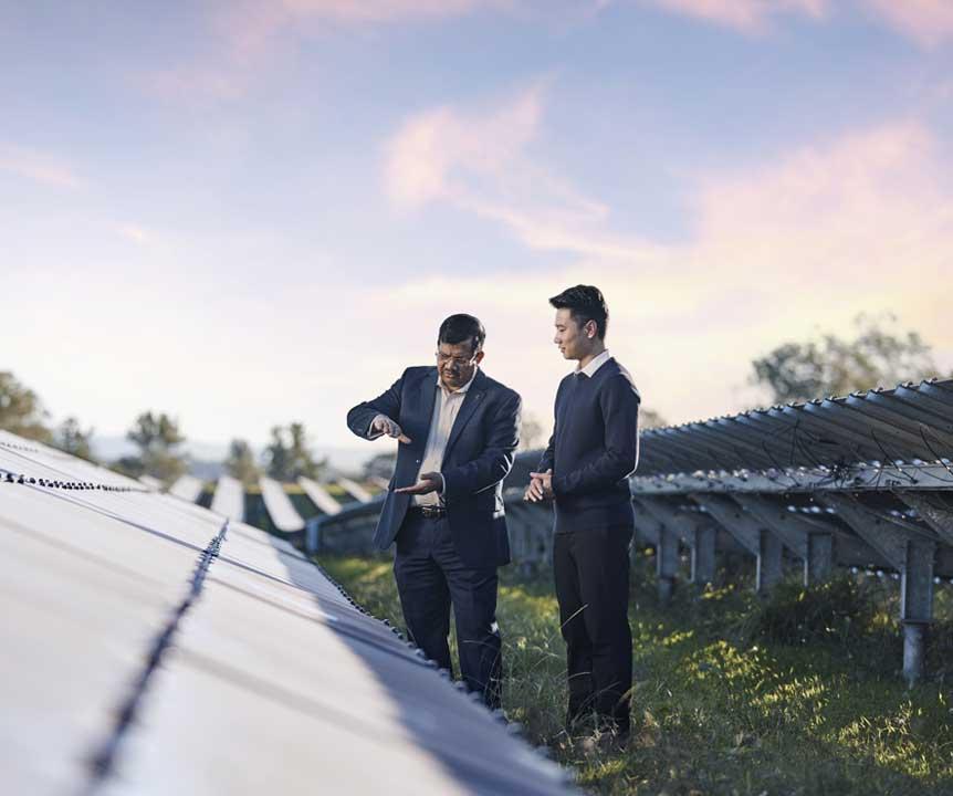 2 UQ researchers assessing a row of solar panels on a sunny day at one of our solar farms