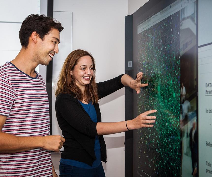Two people using a wall-mounted touchscreen.