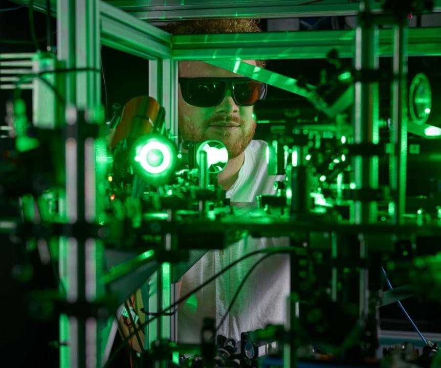 UQ researcher inspects some manufacturing equipment surrounded by green lasers