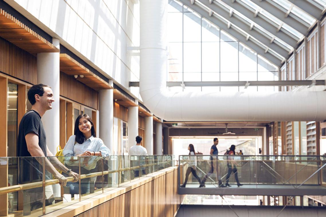 Students standing on the top level of a building with a glass roof above them. 