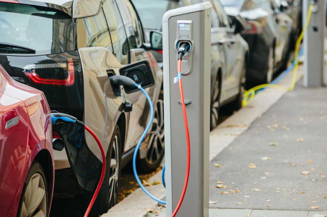 A row of electric vehicles are parked along the street with charging cables plugged in