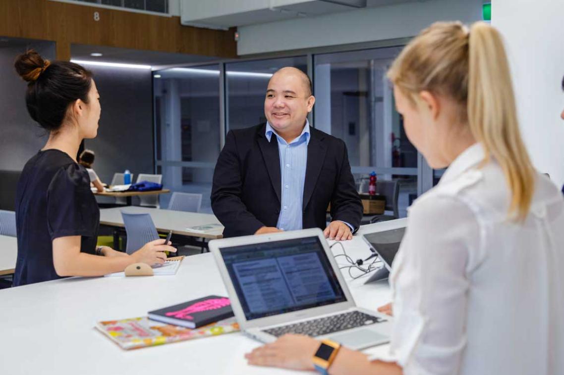 UQ students with laptops and notebooks in conversation with a man in a suit