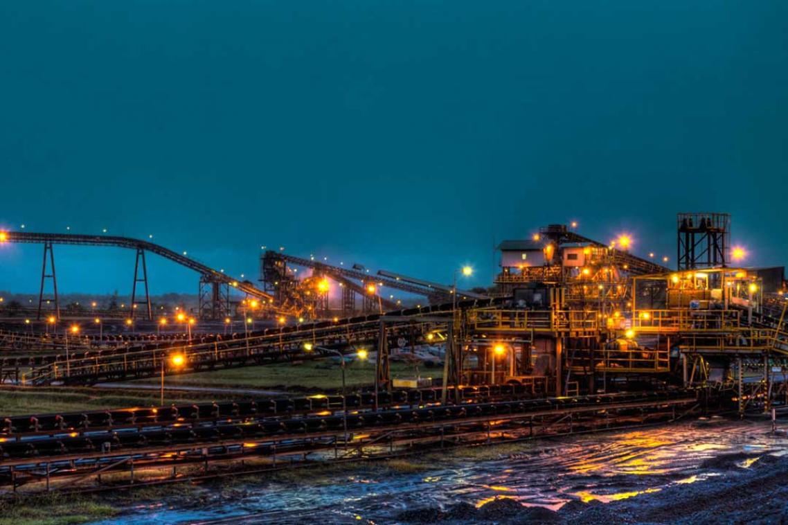Long shot of a coal mine lit up with bright lights at night time.