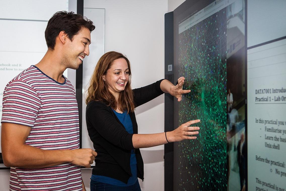 Two people using a wall-mounted touchscreen.