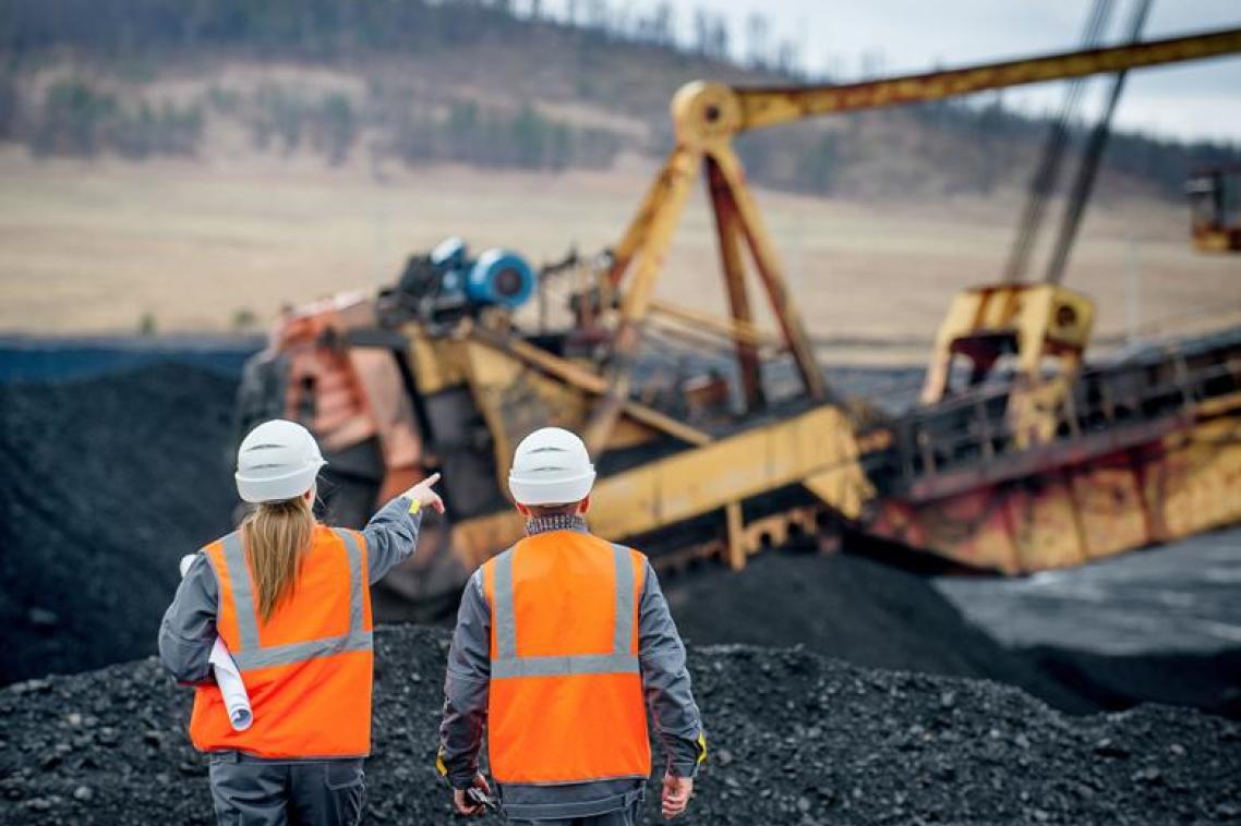 Two people walking on a mine site wearing high-vis and hard hats. Heavy machinery operates in the background.