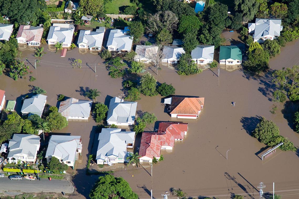 An aerial view of a flooded neighbourhood, with most houses and streets submerged in floodwaters.