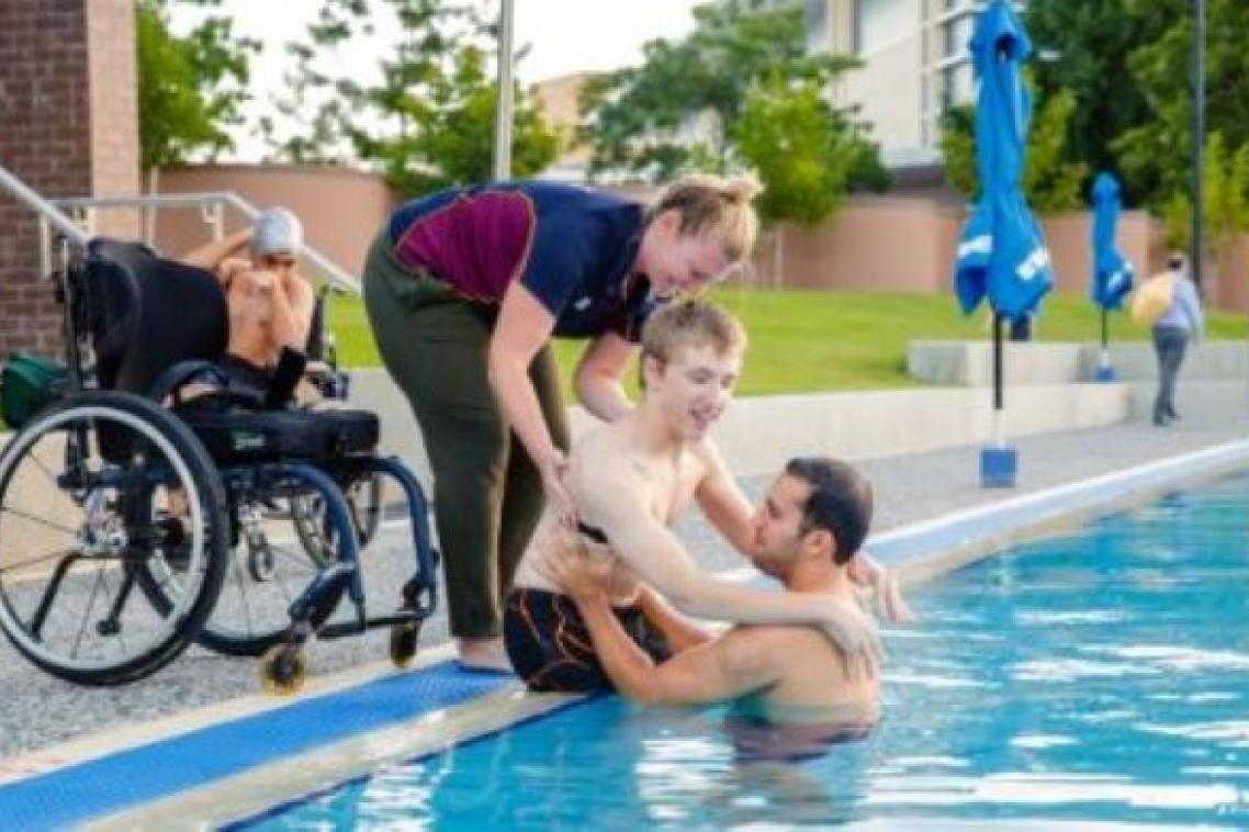 UQ clinicians helping a patient in a wheelchair to enter a swimming pool